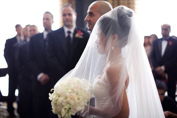 Bride, under a full-length veil, and groom stand at the altar - wedding photo by Melissa Jill Photography